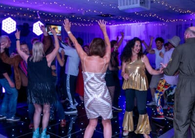 Glamorously dressed guests dancing at a 60th birthday disco in Amersham