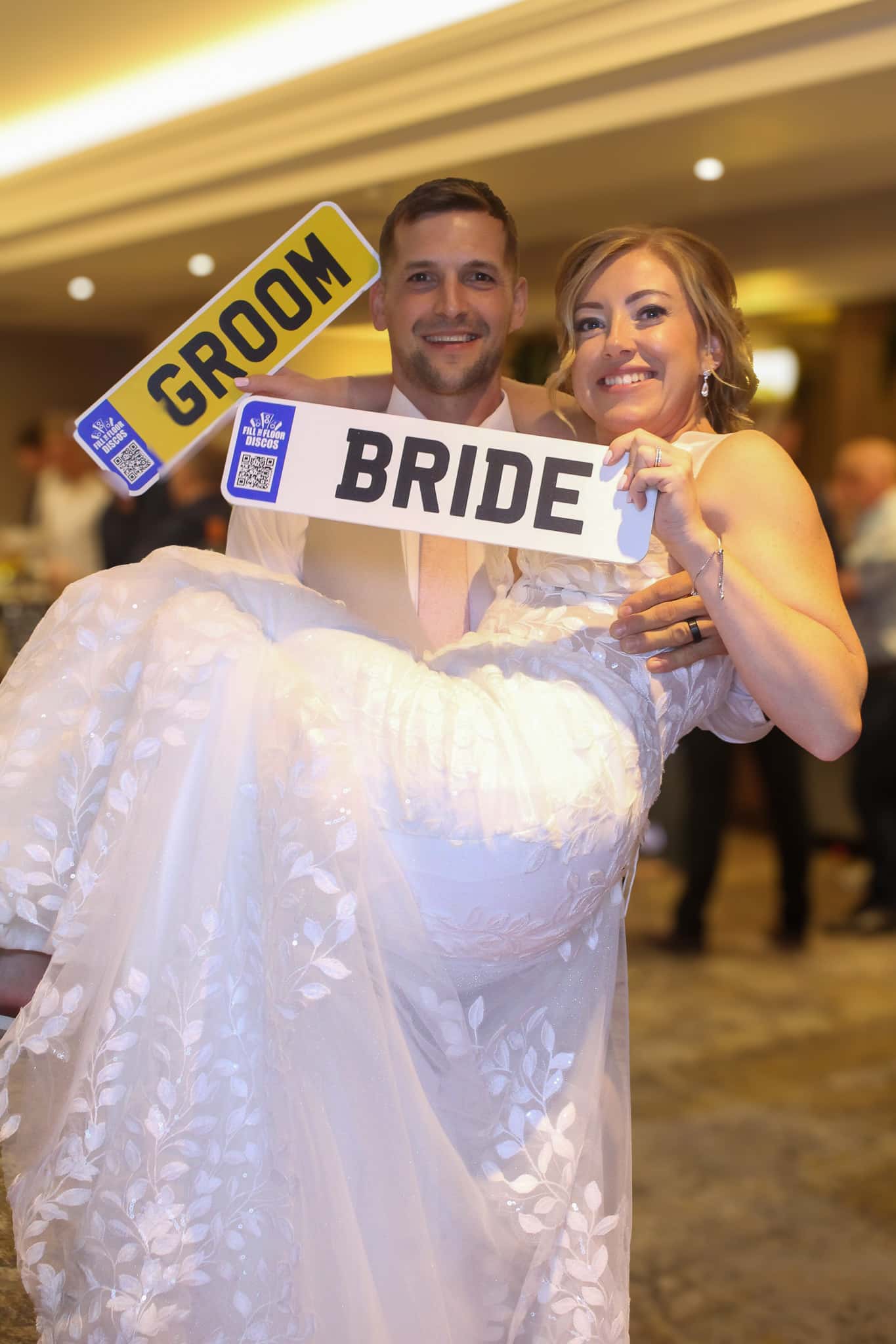 Groom carrying the bride with bride and groom photo booth signs
