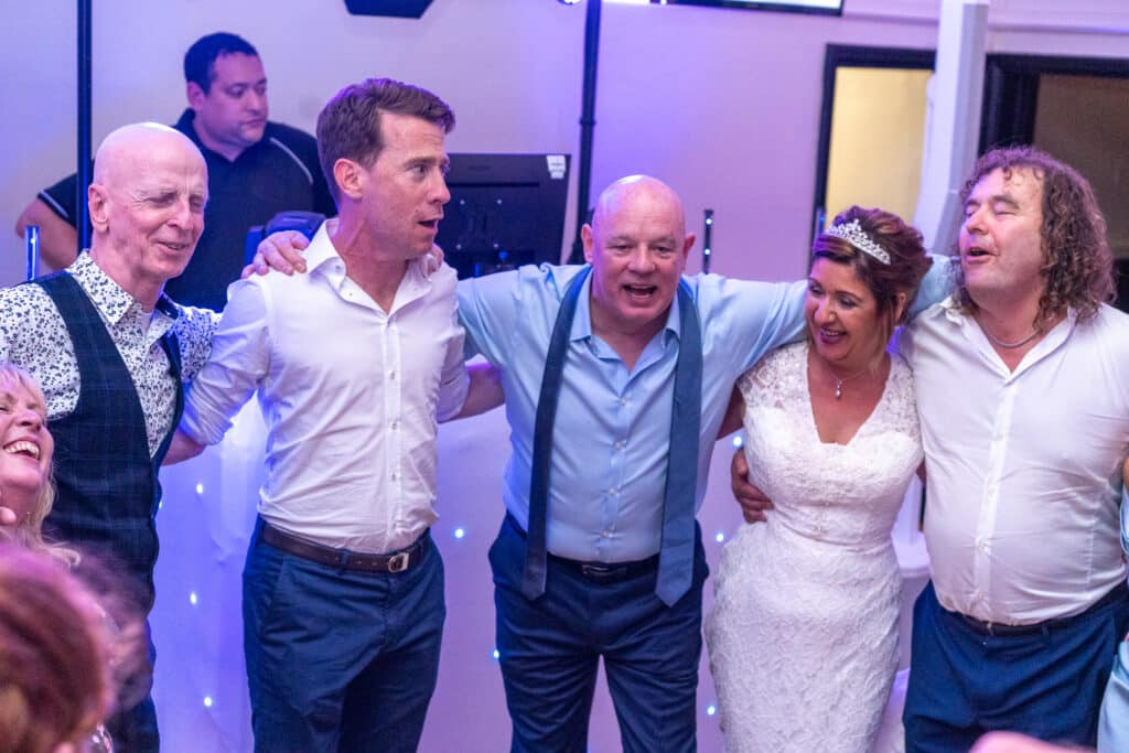 Guests singing arm in arm at Sally&rsquo;s wedding, London Shenley Club