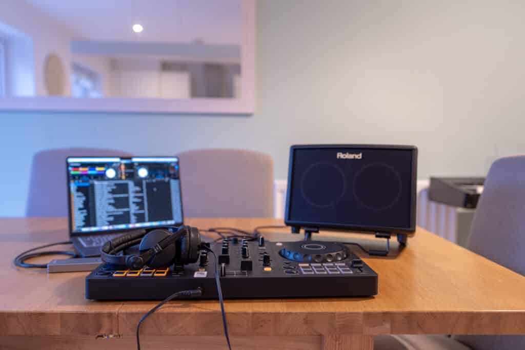 The full DJ lesson setup — controller, laptop, headphones and speaker on an ordinary dining table