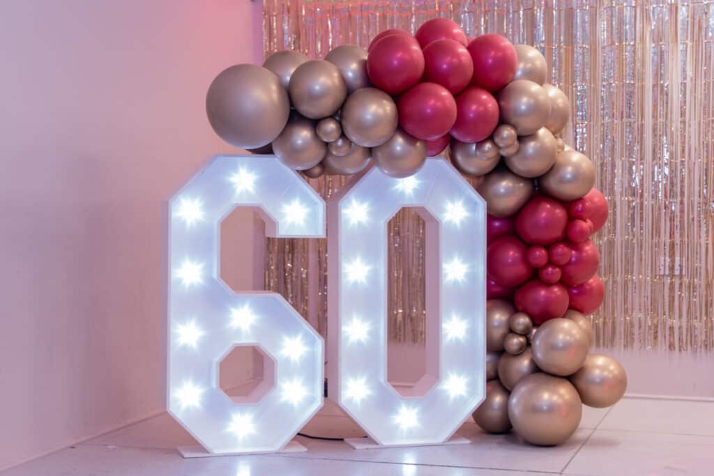 4ft light-up 60 numbers under a balloon arch at Jane's surprise 60th birthday party at Stanbridge & Tilsworth Community Hall