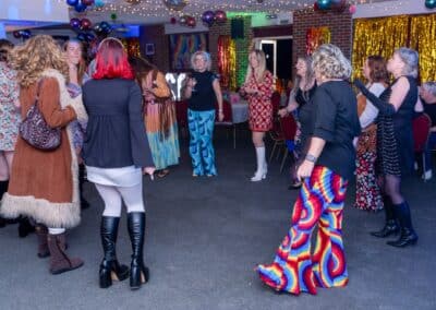 Guests in 60s fancy dress dancing under balloons and gold tinsel at Lisa's 60th at Amersham & Chiltern Rugby Club
