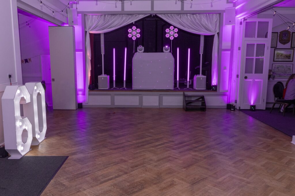 White DJ setup on the stage with the 4ft light-up 60 numbers to the side of the hall at Mark and Paula’s joint 60th at Wingrave Community Centre